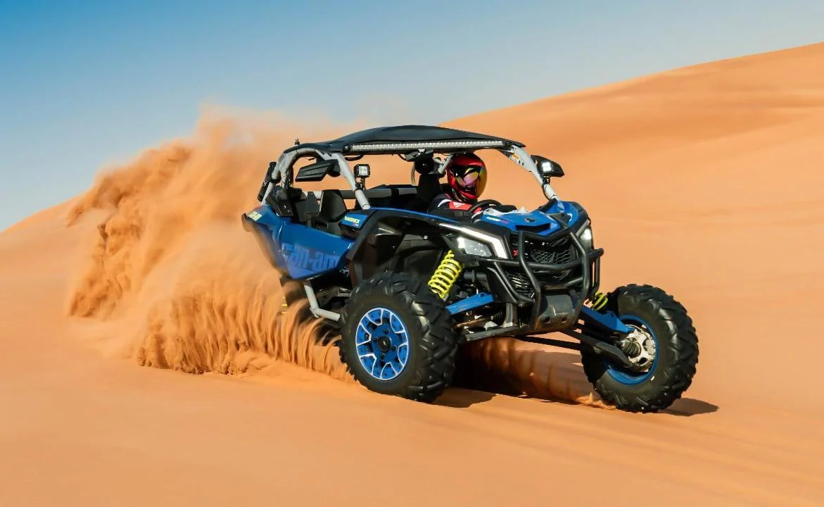 Blue Can-Am Maverick driving across desert dunes